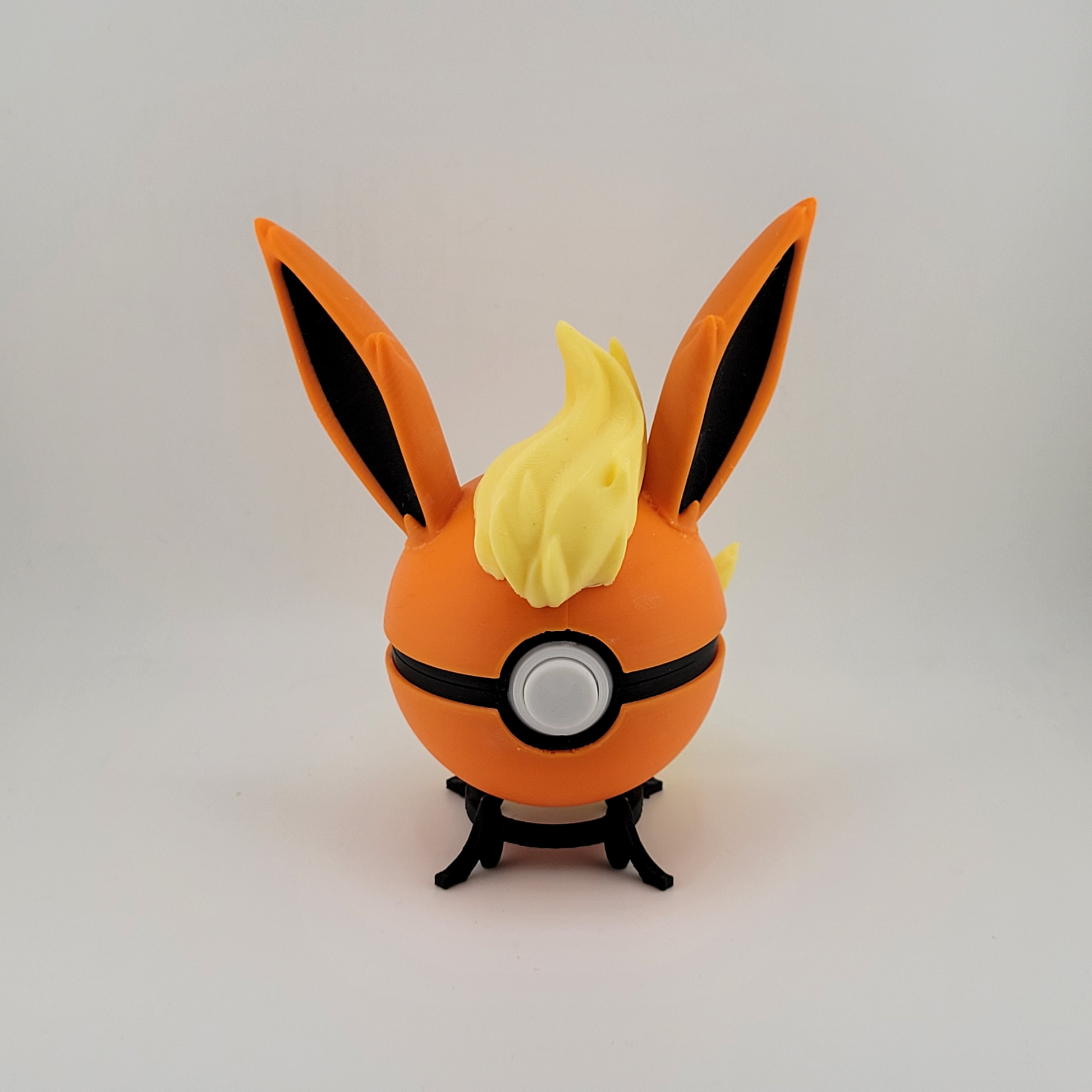 Flareon Pokeball with orange and yellow design featuring ears and tuft, displayed on a stand.