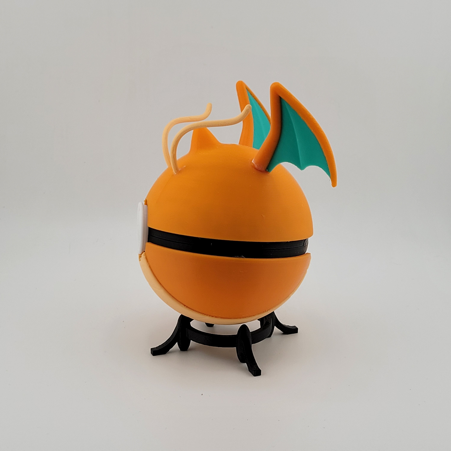 Dragonite-themed Poké Ball with orange hue and wing details on display stand.