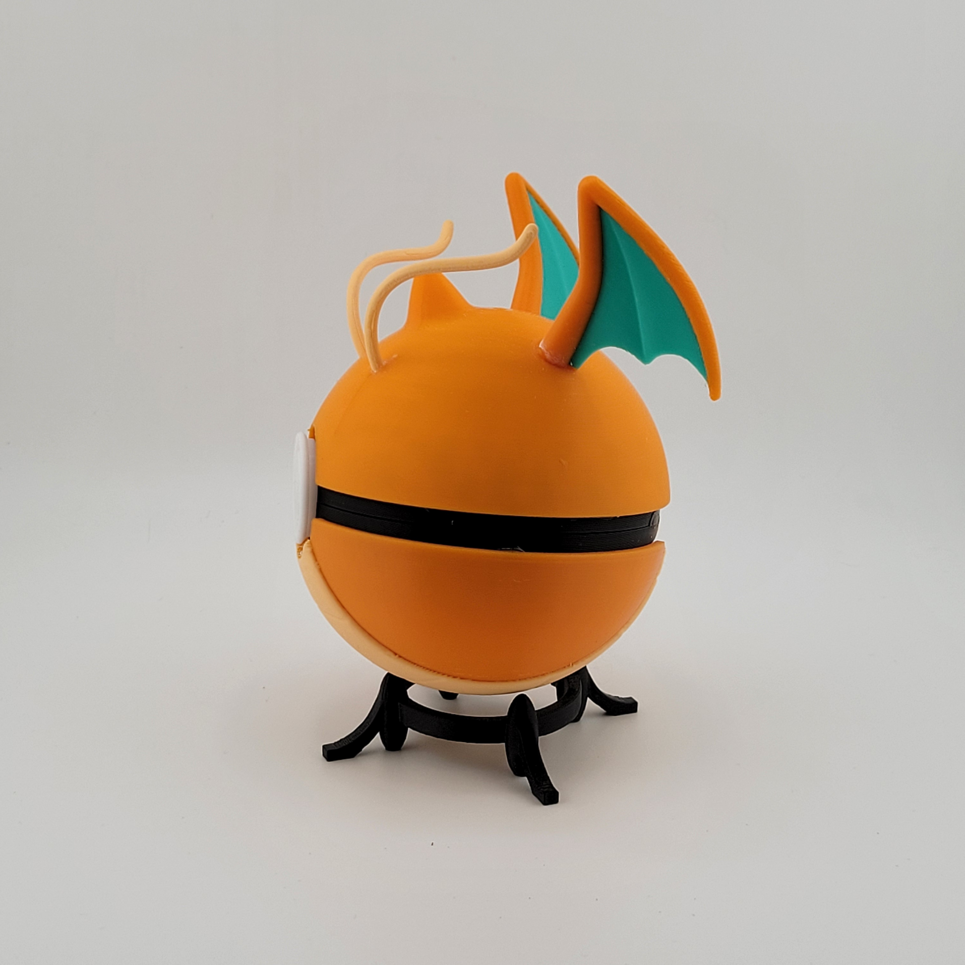 Dragonite-themed Poké Ball with orange hue and wing details on display stand.