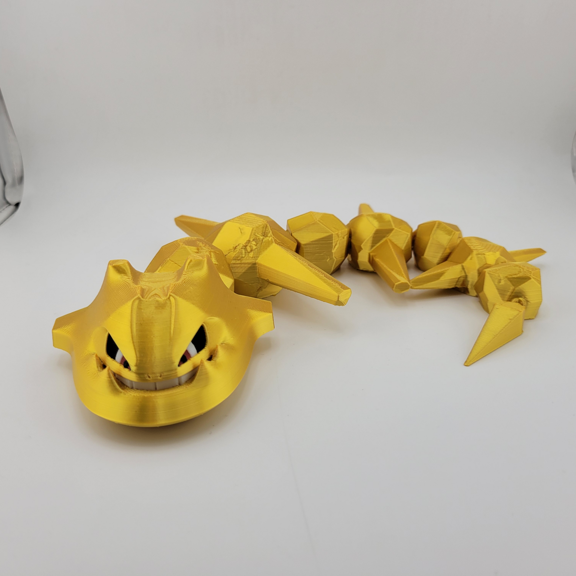 Articulated Steelix 3D printed Pokémon toy in golden color on a white background.