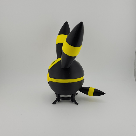 3D printed Umbreon-themed Pokéball with black and yellow design, featuring ears and tail, displayed on a small black stand against a plain white background.