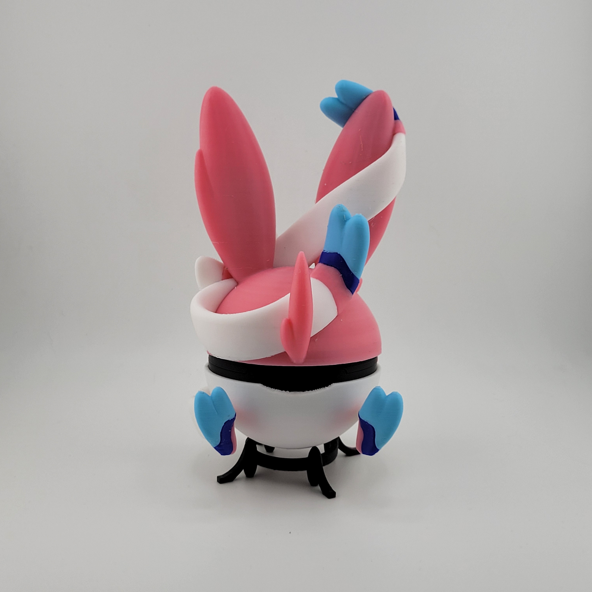 3D printed Sylveon-themed Pokéball with pastel pink, blue, and white colors and ribbon motifs, handcrafted collectible display.
