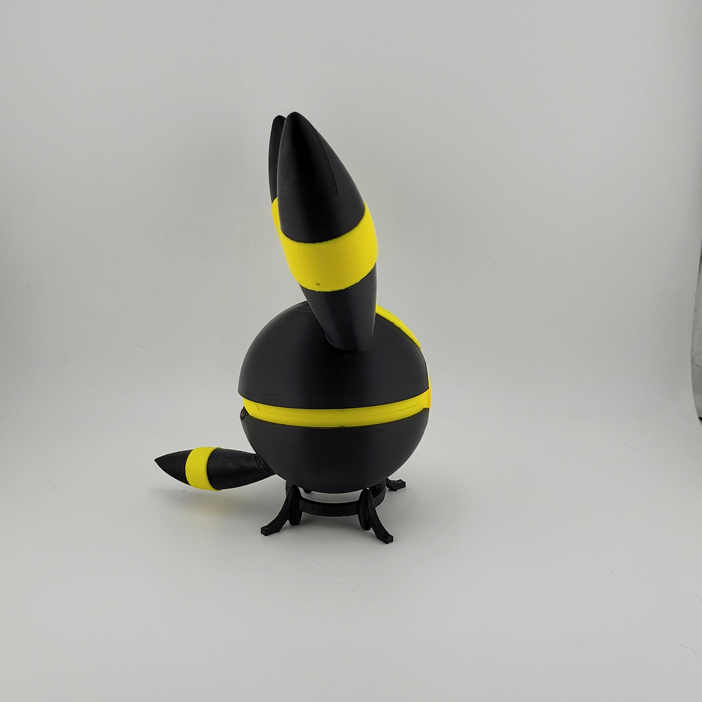 3D printed Umbreon-themed Pokéball in black with yellow rings, featuring a latch-style button and standing on a small black stand.