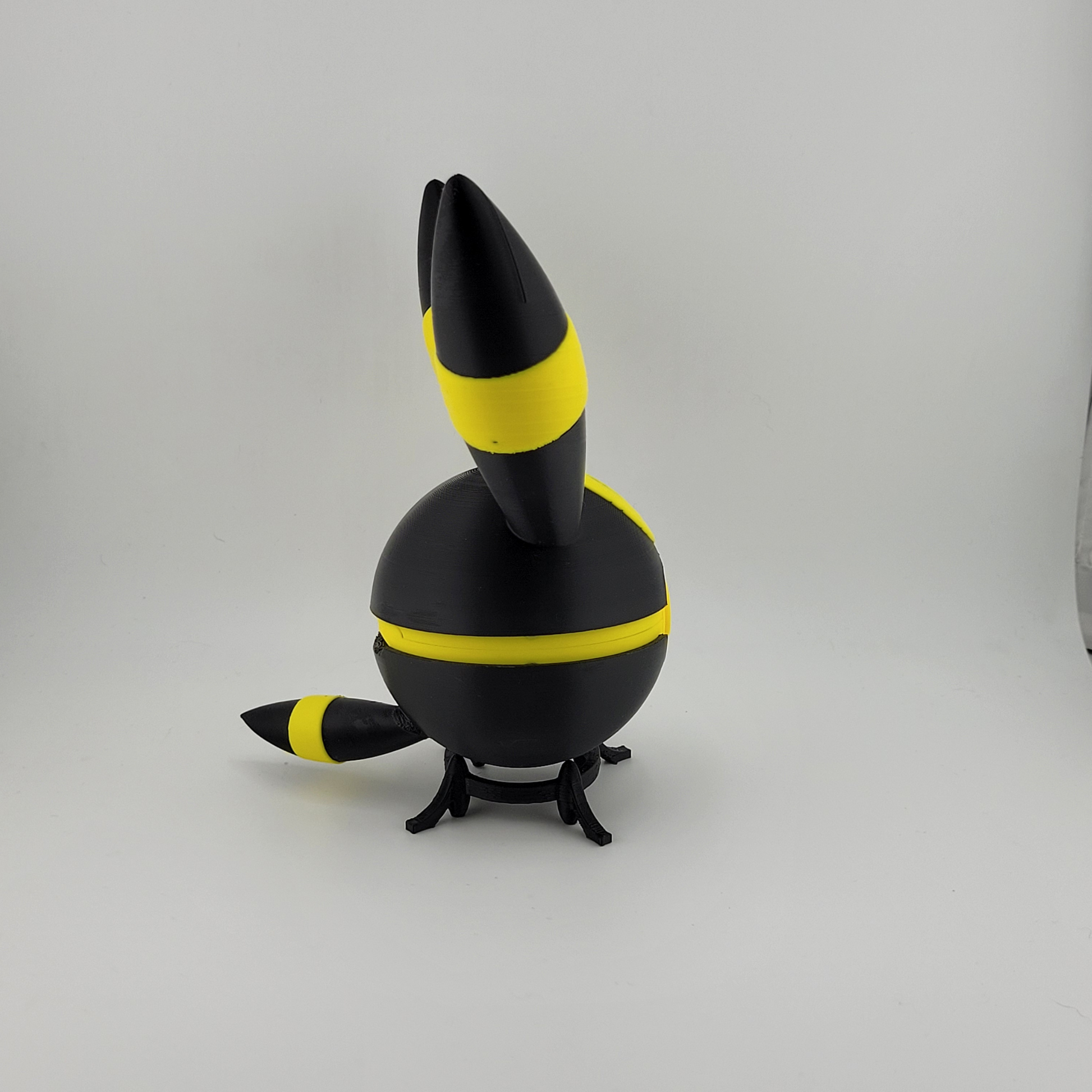 3D printed Umbreon-themed Pokéball in black with yellow rings, featuring a latch-style button and standing on a small black stand.
