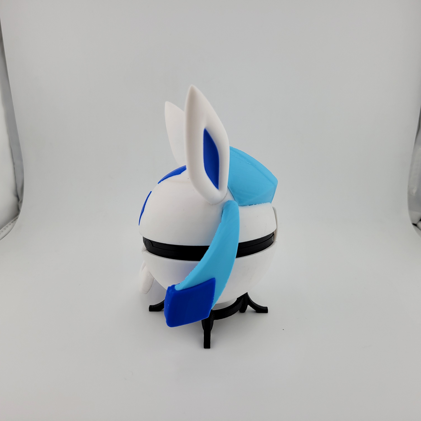 3D printed Glaceon-inspired Poké Ball with blue and white icy design and ear details on a black stand