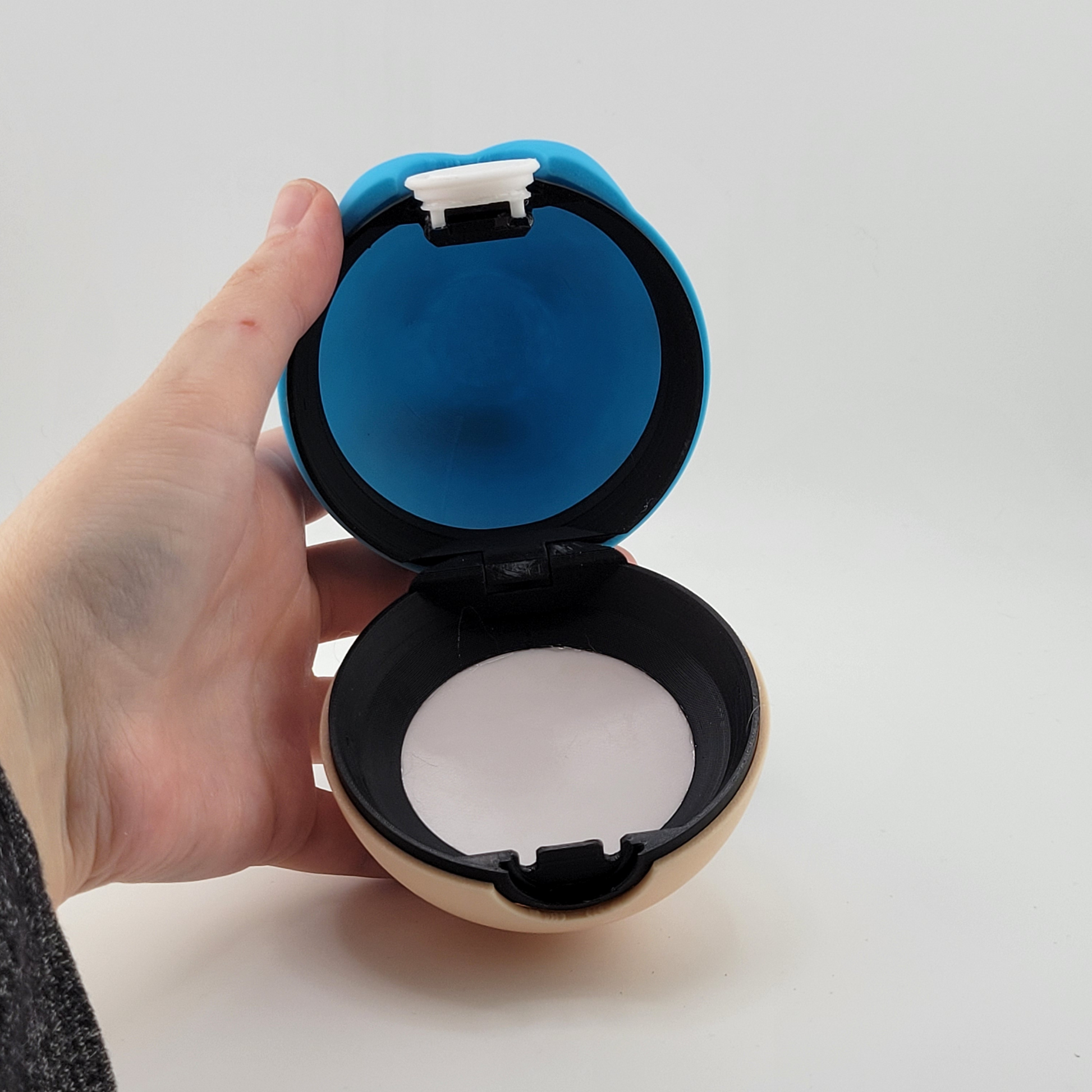 Open Spheal Pokeball held in hand, featuring a blue and cream color scheme with latch mechanism.