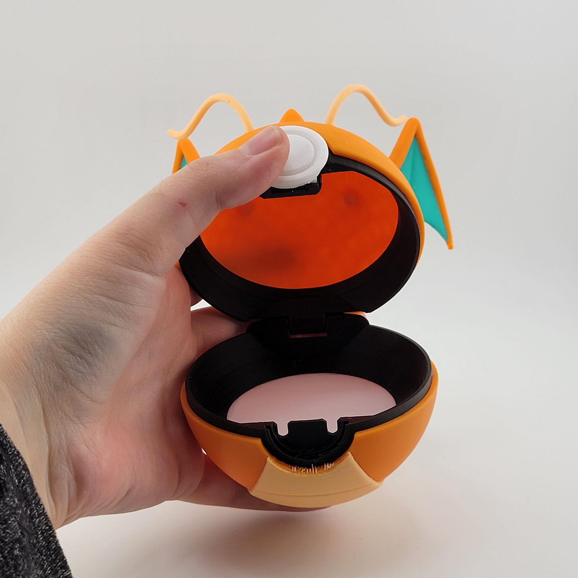 Dragonite-themed Poké Ball open, showcasing its orange design and wing details, held in hand for display.