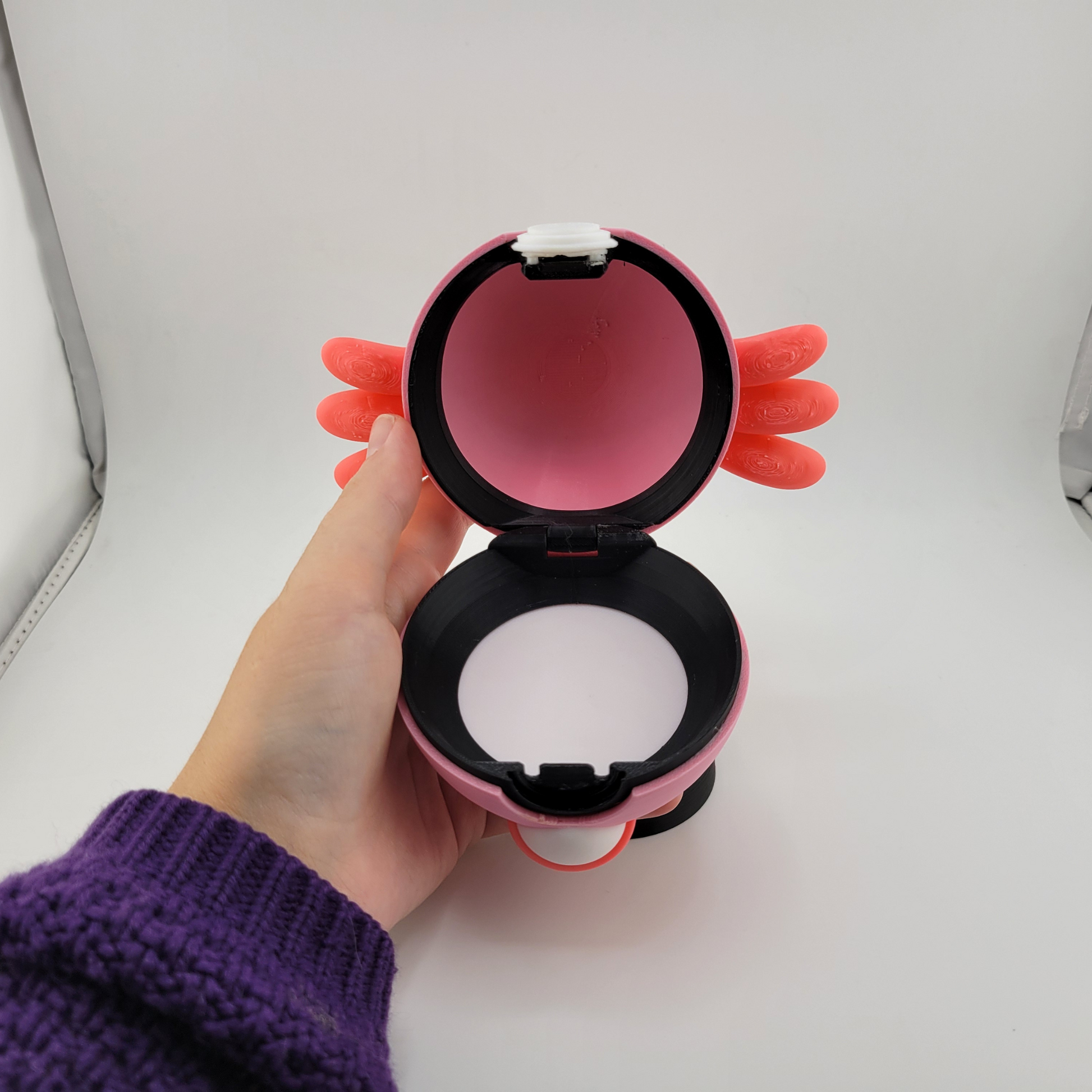 Handheld open Chansey-themed Pokeball 3D printed collectible with pink and black colors and orange wing accents.