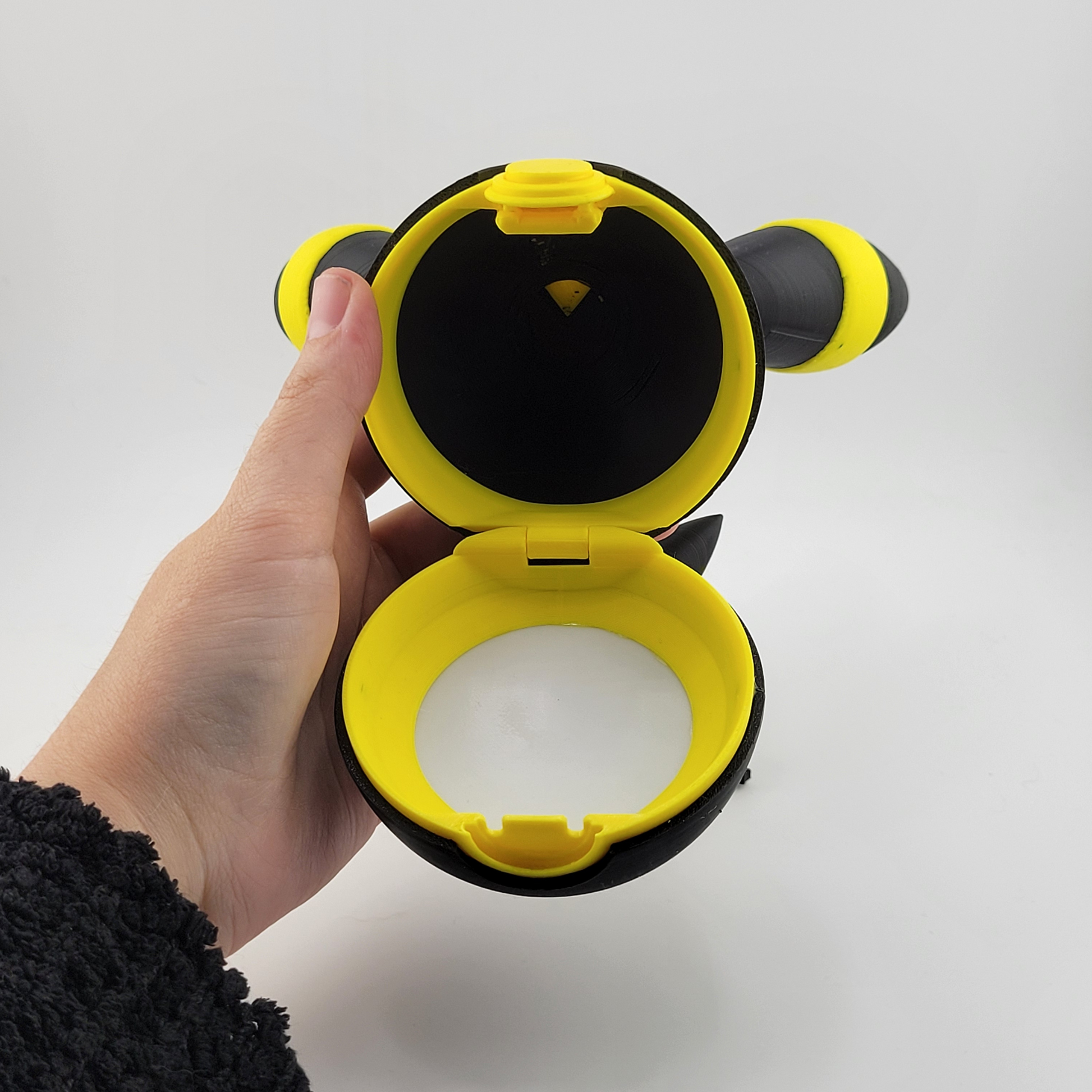 Hand holding an open Umbreon-themed Pokéball with black exterior and glowing yellow rings, showing interior compartments against a white background.