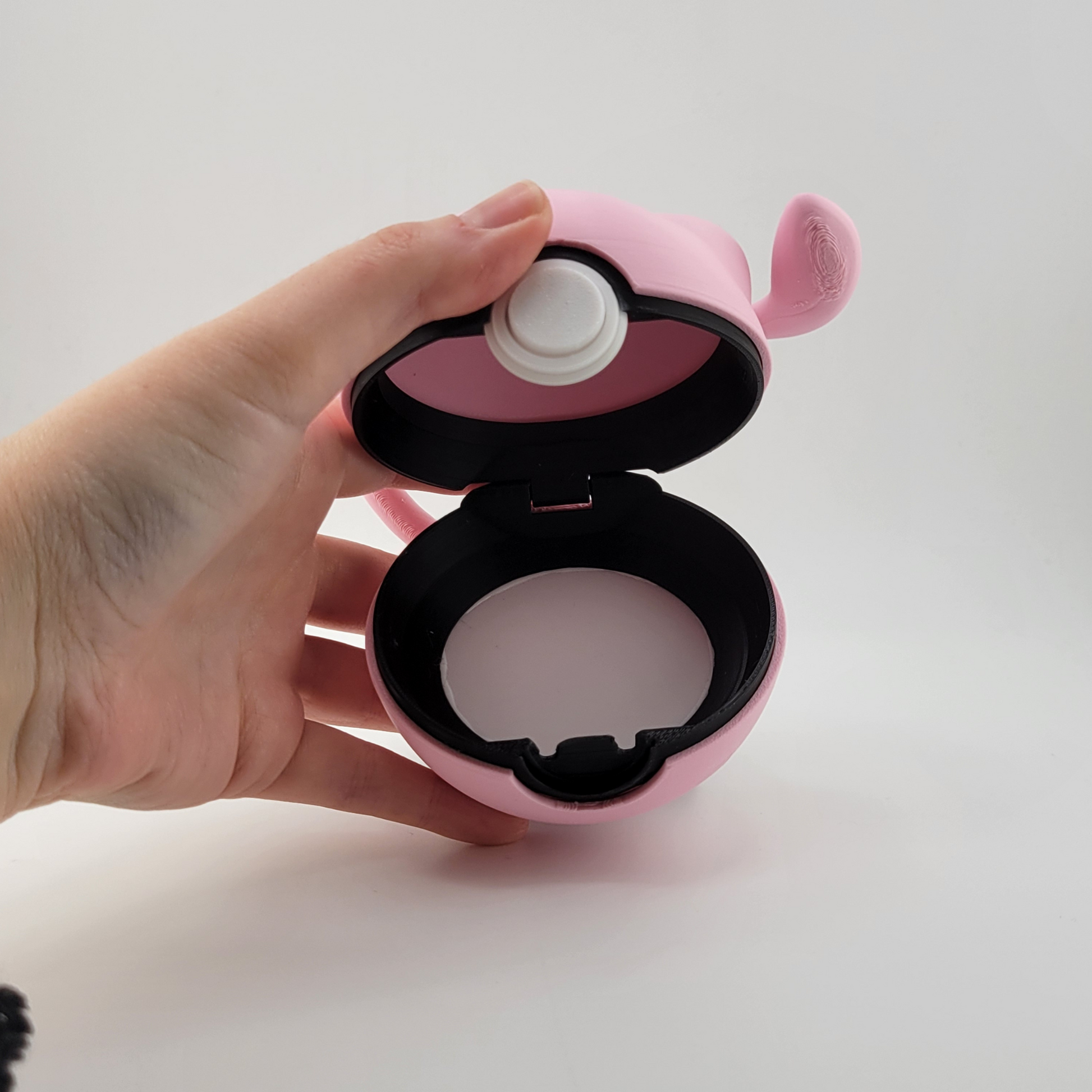 Pink Mew-themed Pokéball with tail, open to show interior, held in hand.