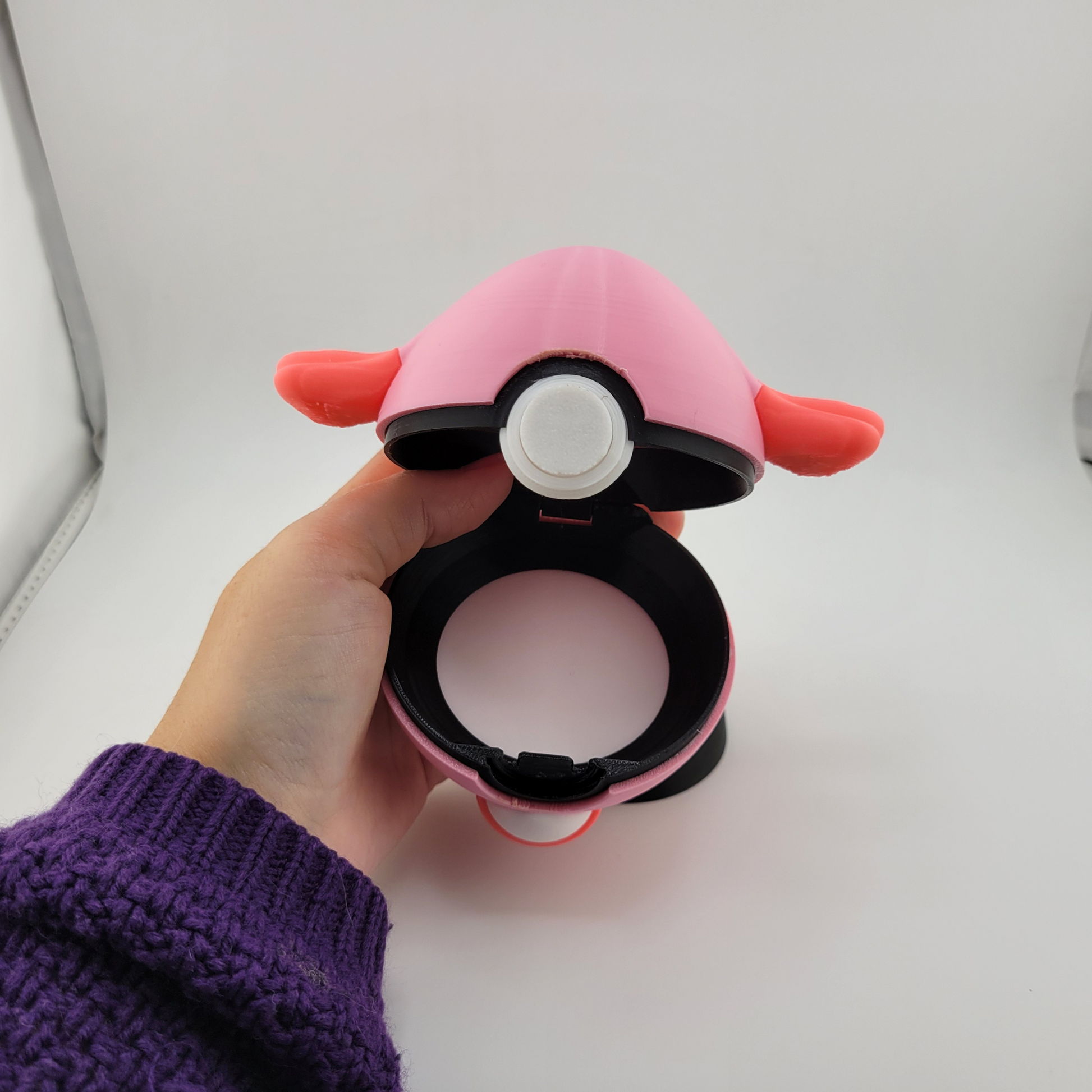 Hand holding a pink Chansey-themed Pokeball made of durable PLA plastic, open to show the interior latch mechanism, designed for display and gentle play.