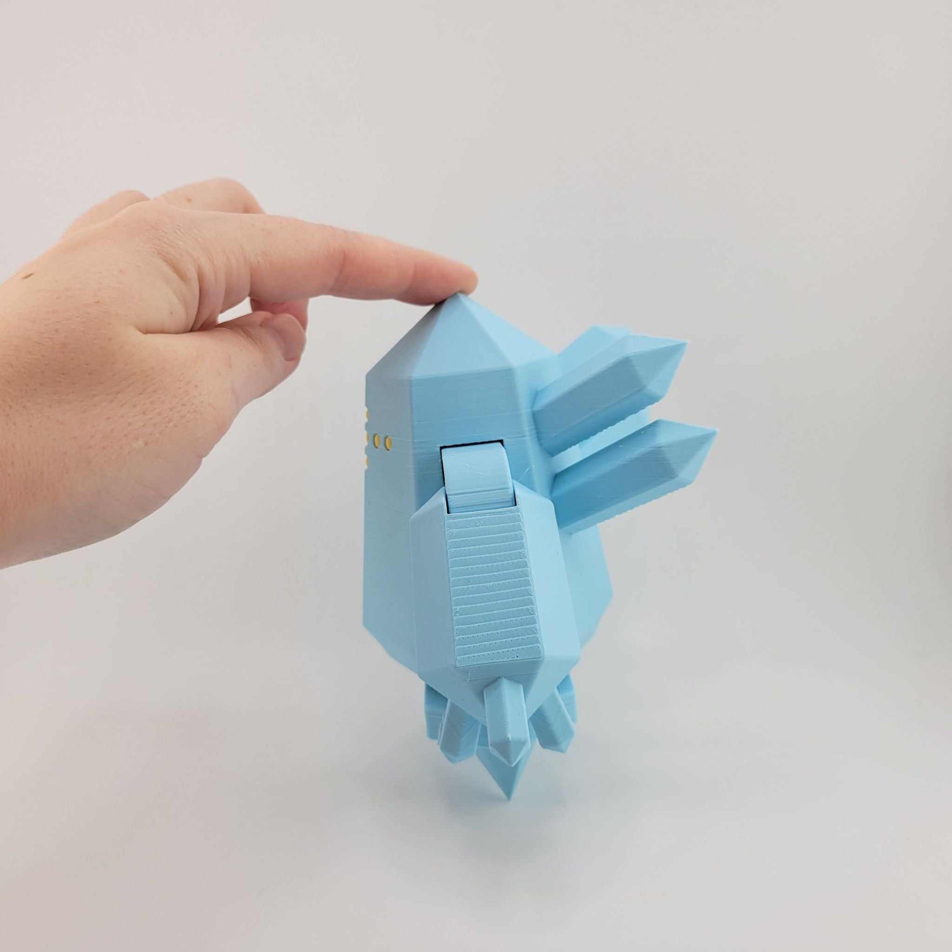 Hand holding a small, light blue 3D printed articulated Regice figure from Pokémon against a plain white background