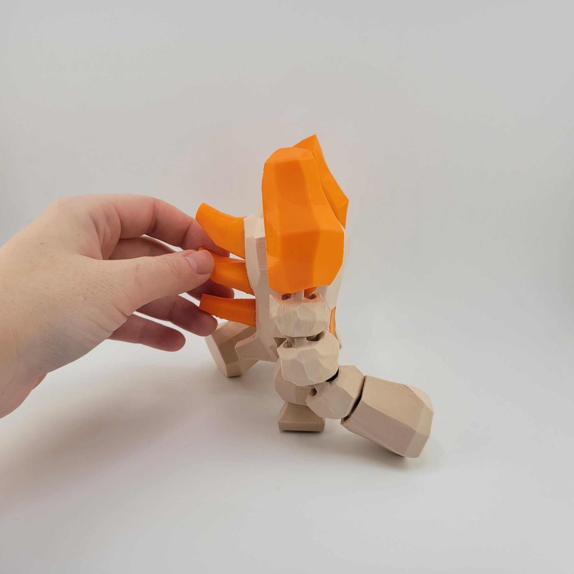 3D printed poseable Regirock figure with articulated arms in orange and beige, held by a hand against a plain white background