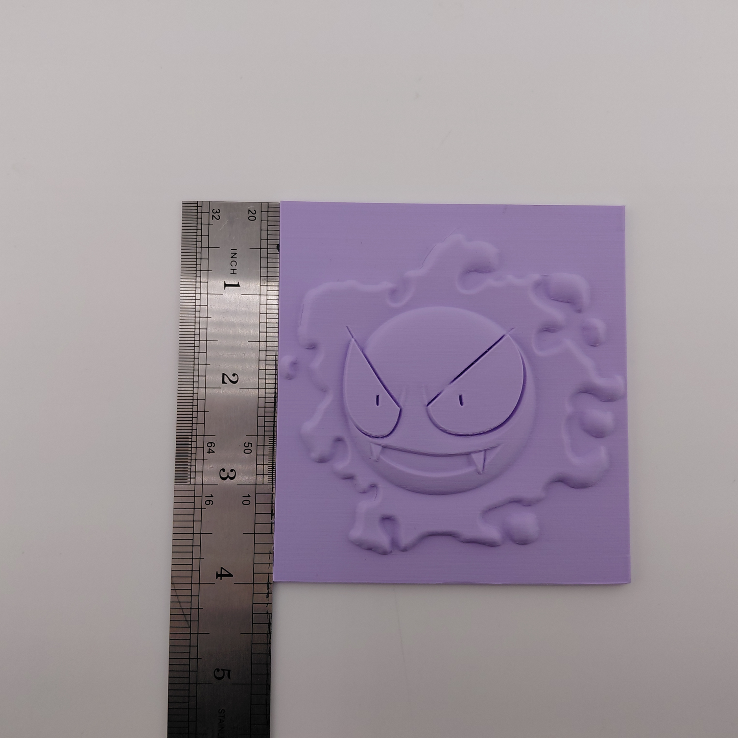 Set of three lavender 3D printed relief plaques featuring Gastly, Haunter, and Gengar inspired ghost monsters displayed on black stands against a white background. Each square plaque has raised detailed artwork and comes with its own stand for desk, shelf, or gaming room decor. Available individually or as a matching set for collectors and fans of spooky monster-inspired decor.