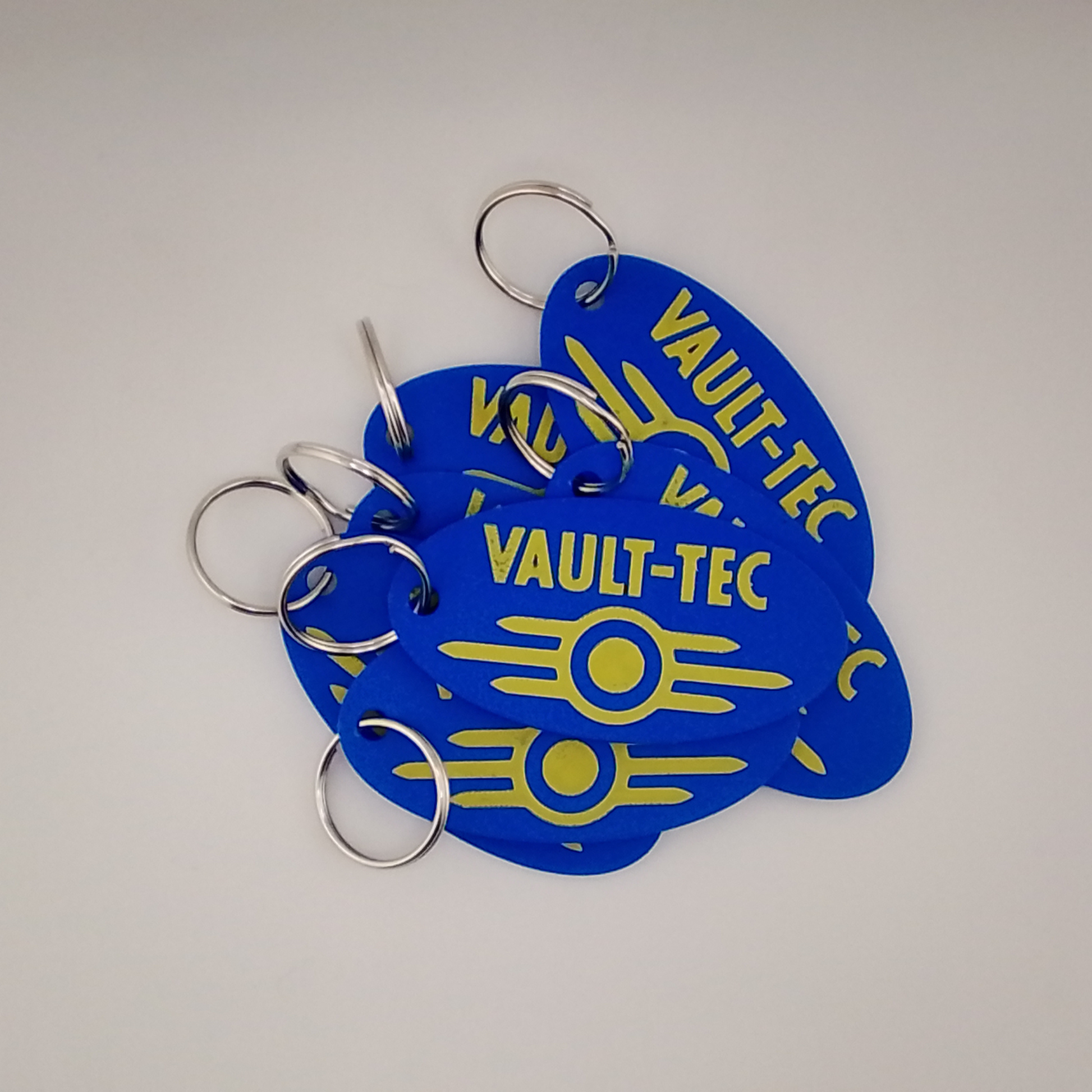 Blue 'Vault-Tec' keychains with yellow text on a white background
