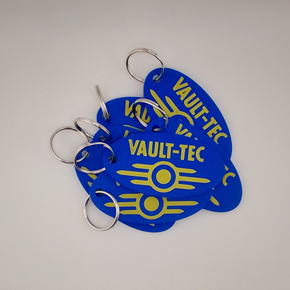Blue 'Vault-Tec' keychains with yellow text on a white background