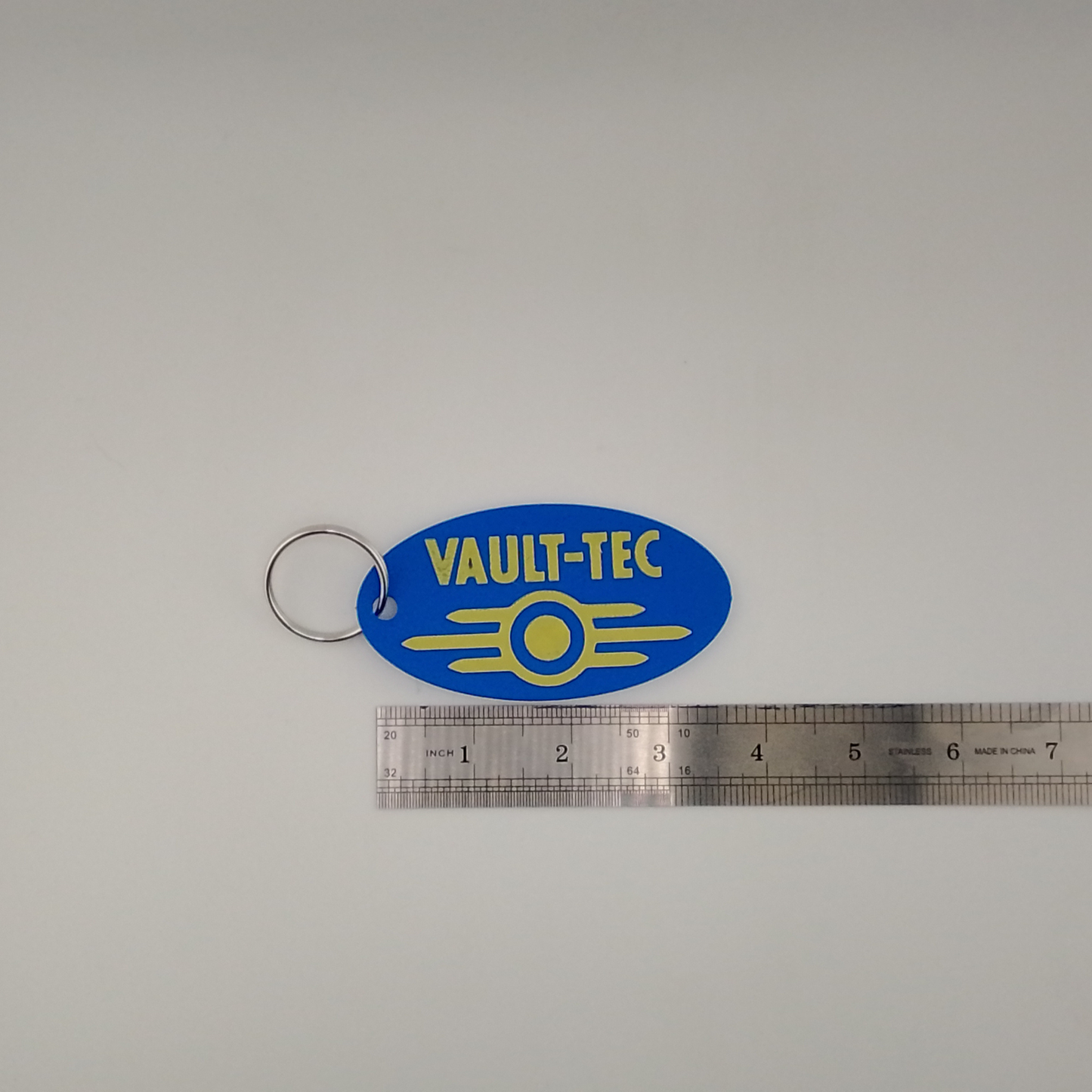 Vault-Tec keychain with a ruler for scale on a gray background