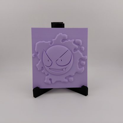 Set of three lavender 3D printed relief plaques featuring Gastly, Haunter, and Gengar inspired ghost monsters displayed on black stands against a white background. Each square plaque has raised detailed artwork and comes with its own stand for desk, shelf, or gaming room decor. Available individually or as a matching set for collectors and fans of spooky monster-inspired decor.