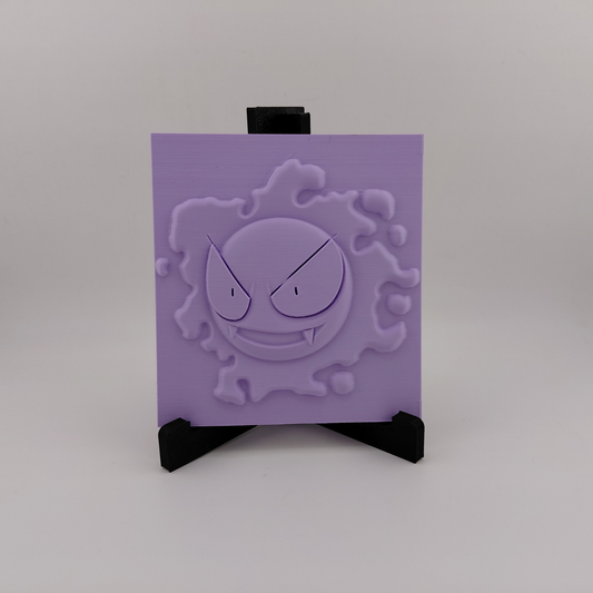 Set of three lavender 3D printed relief plaques featuring Gastly, Haunter, and Gengar inspired ghost monsters displayed on black stands against a white background. Each square plaque has raised detailed artwork and comes with its own stand for desk, shelf, or gaming room decor. Available individually or as a matching set for collectors and fans of spooky monster-inspired decor.