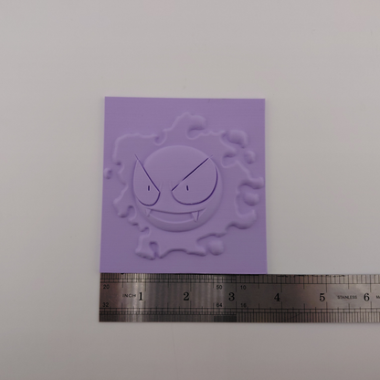 Set of three lavender 3D printed relief plaques featuring Gastly, Haunter, and Gengar inspired ghost monsters displayed on black stands against a white background. Each square plaque has raised detailed artwork and comes with its own stand for desk, shelf, or gaming room decor. Available individually or as a matching set for collectors and fans of spooky monster-inspired decor.