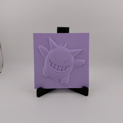Set of three lavender 3D printed relief plaques featuring Gastly, Haunter, and Gengar inspired ghost monsters displayed on black stands against a white background. Each square plaque has raised detailed artwork and comes with its own stand for desk, shelf, or gaming room decor. Available individually or as a matching set for collectors and fans of spooky monster-inspired decor.