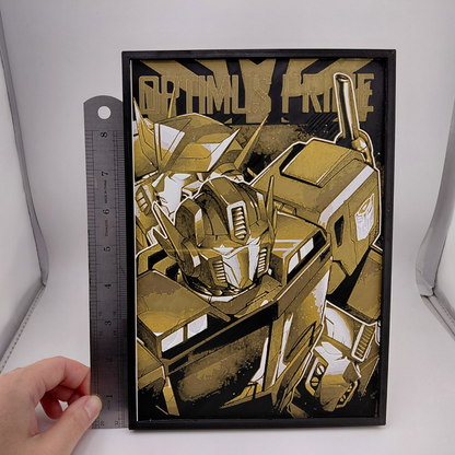 Layered 3D printed Optimus Prime wall art inspired by a classic Transformers comic cover. Created using Chroma Canvas technology with textured depth, lightweight PLA construction, black frame, and gold, black, and white color palette. Can be displayed on a desk using the built-in stand or hung on a wall. Ideal for Transformers collectors, comic fans, gaming rooms, and nerd office décor.