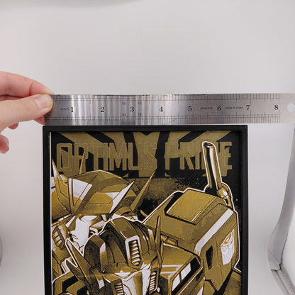 Layered 3D printed Optimus Prime wall art inspired by a classic Transformers comic cover. Created using Chroma Canvas technology with textured depth, lightweight PLA construction, black frame, and gold, black, and white color palette. Can be displayed on a desk using the built-in stand or hung on a wall. Ideal for Transformers collectors, comic fans, gaming rooms, and nerd office décor.